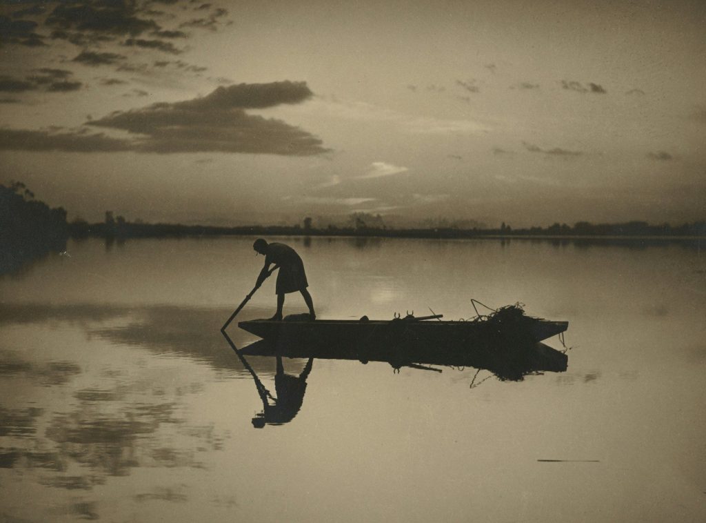 Fotografía vintage en blanco y negro de un pescador solitario remando en su barca, envuelto en la bruma de un paisaje invernal texturizado por el paso del tiempo.