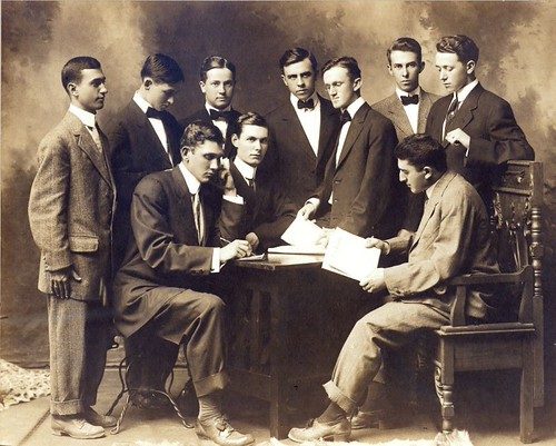 Retrato en sepia del equipo de redacción de Chronicle Staff, hacia 1908-1911, posando formalmente con trajes y sombreros en una sala de redacción de principios de siglo.